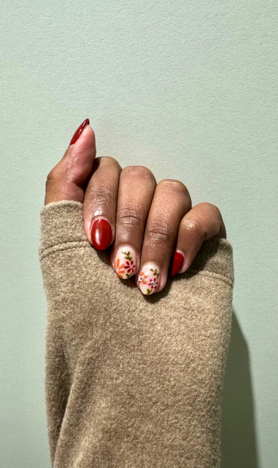 Deep-red nails with two floral-art accent nails, sage-green wall