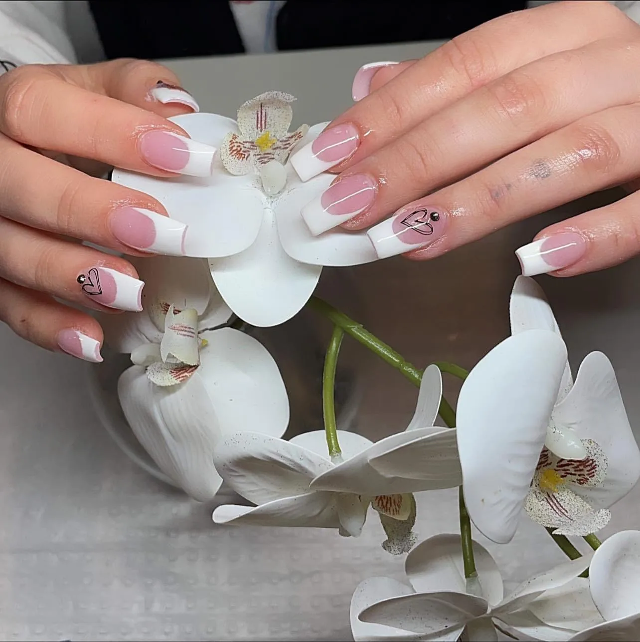 White French tips with heart line-art cradling white orchids — Minack Beauty nail work