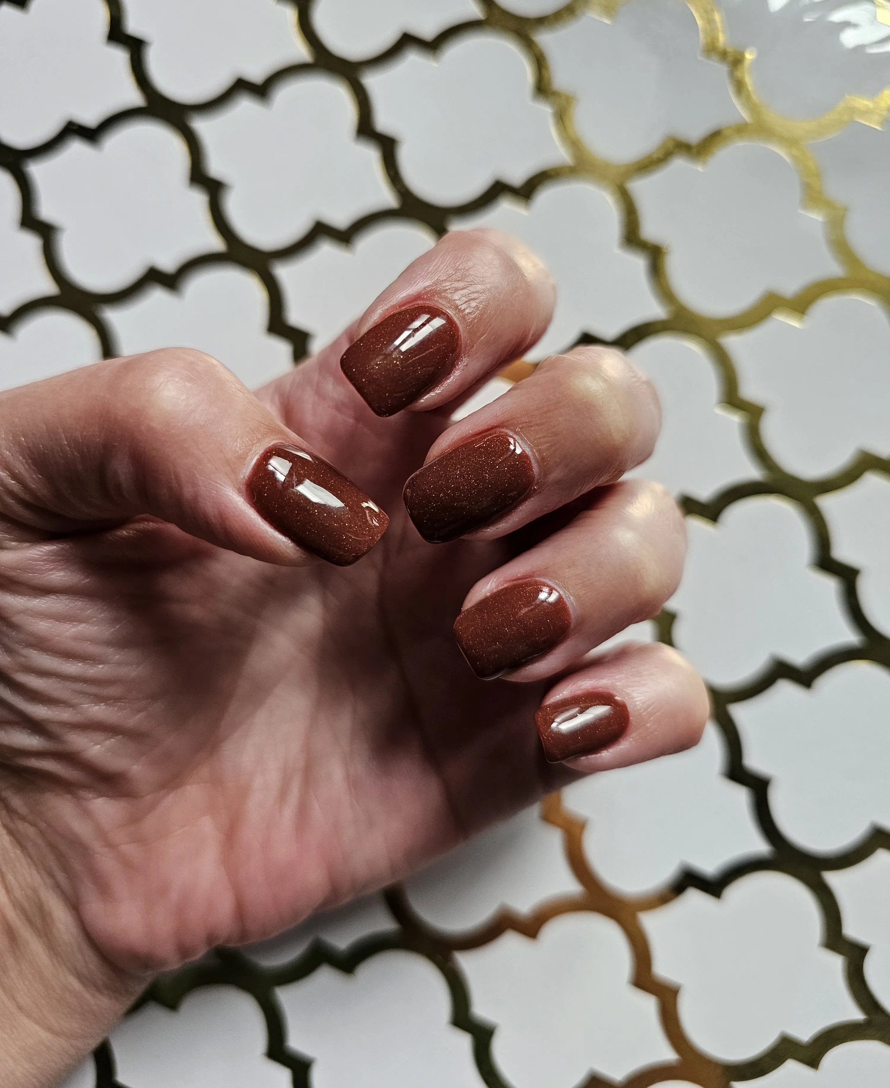 Copper-brown glitter gel square nails on a white-and-gold tile backdrop — Minack Beauty nail work