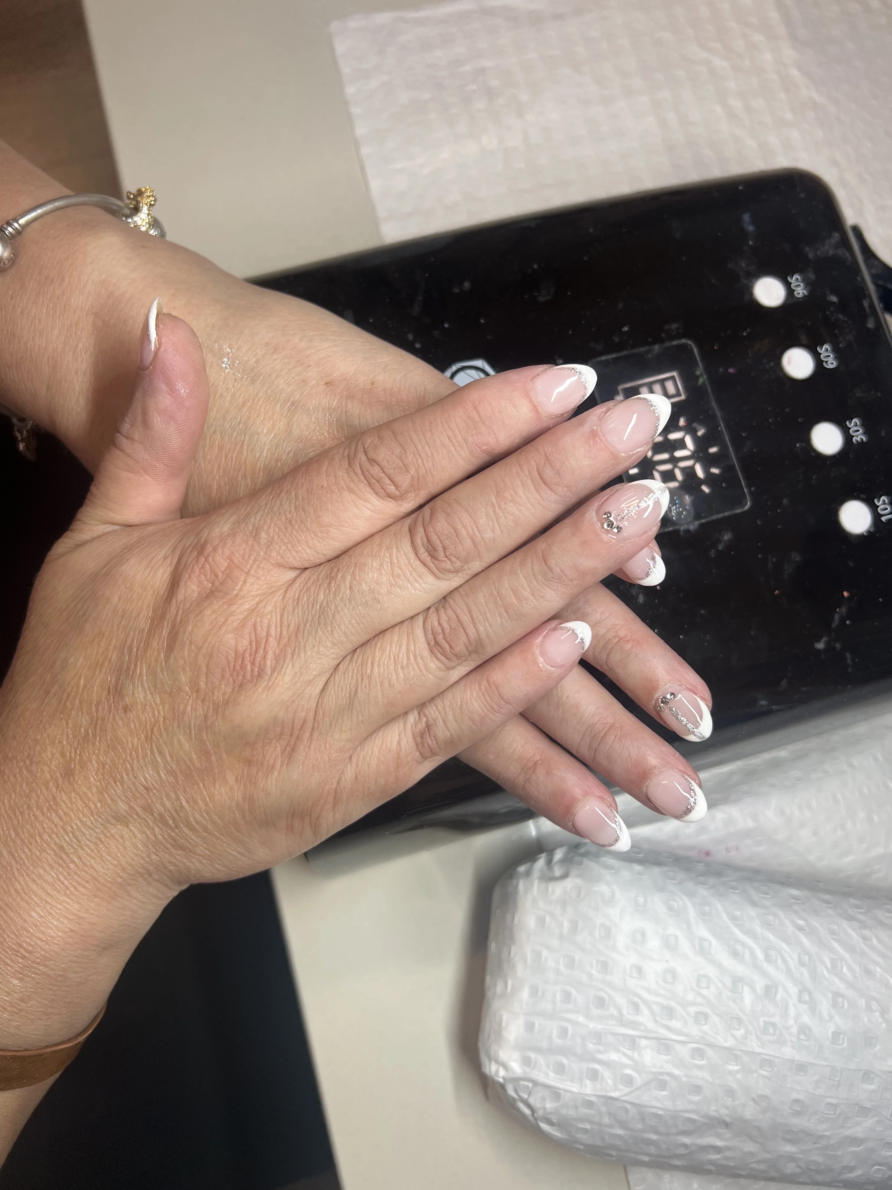 French tips with silver glitter lines and gem accents on a UV lamp